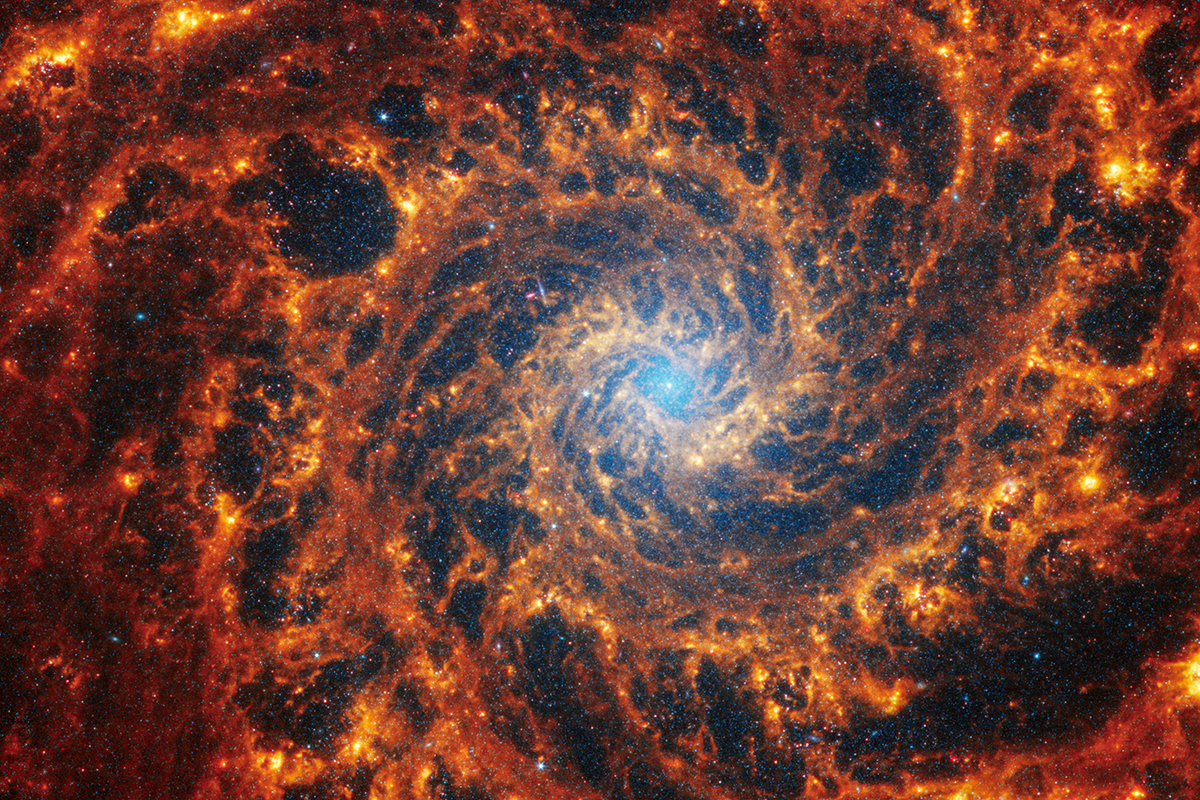A dramatic spiral galaxy with orange and red arms and a light blue center
