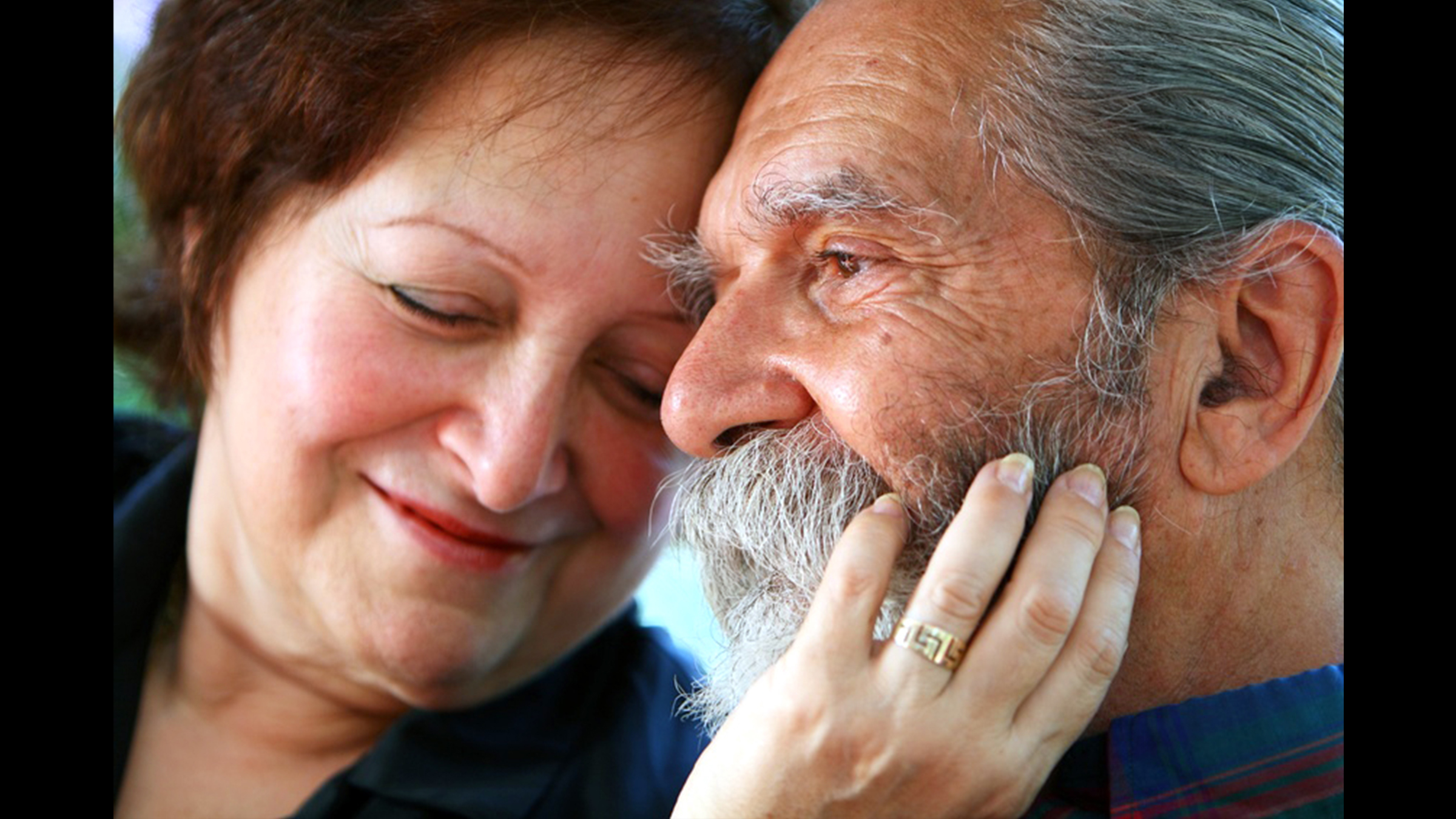 Older couple, the woman's hand rests on the cheek of the man, both look content