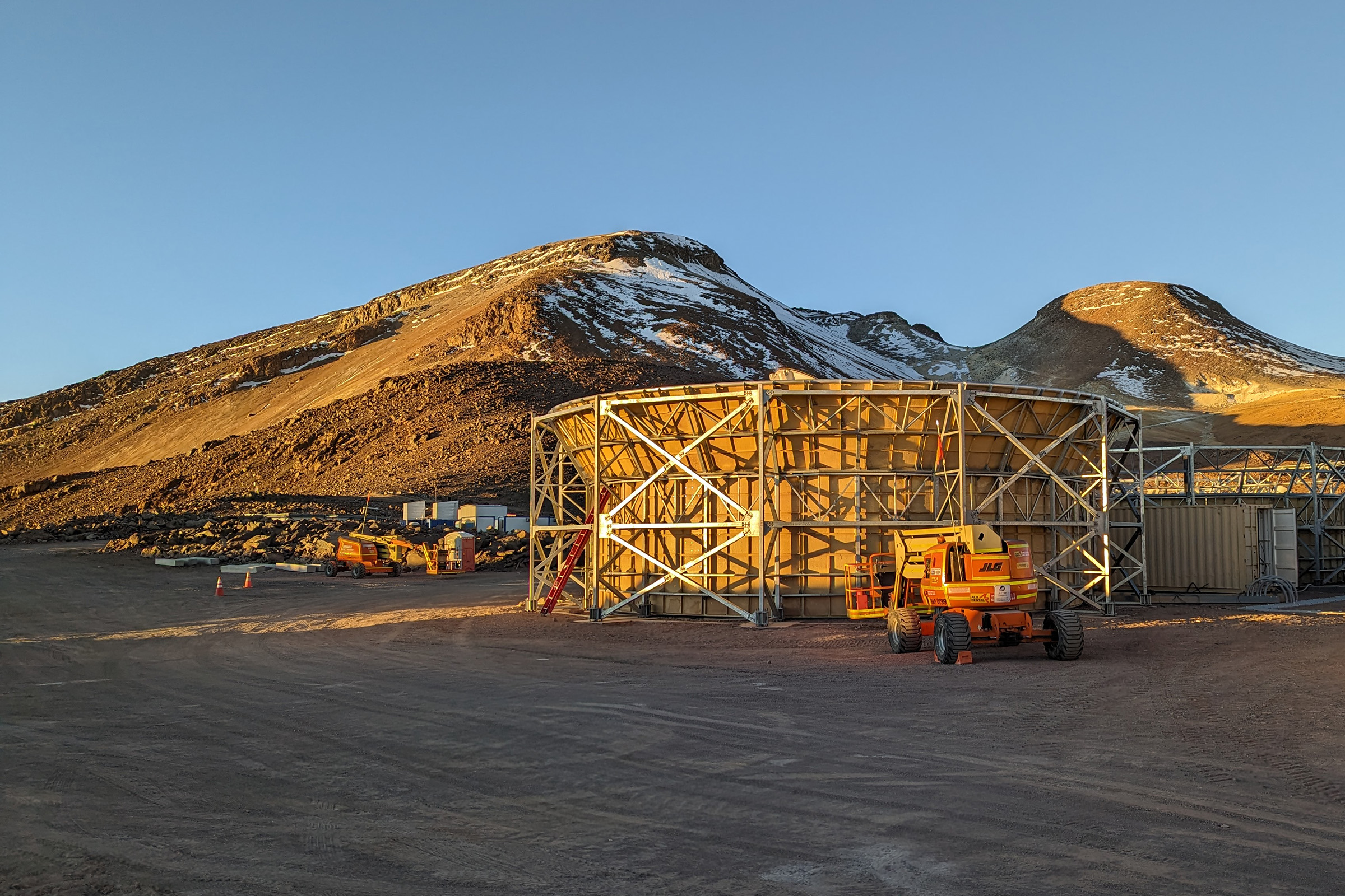 A telescope enclosure sits in front of mountains under a blue sky