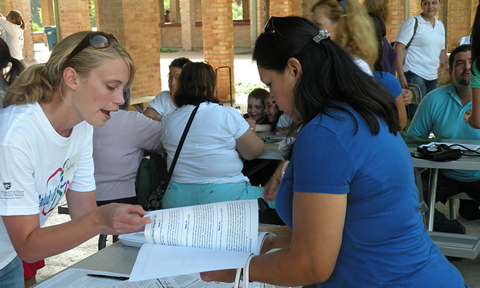 A woman on the left speaks with a woman on the right pointing out info in a booklet